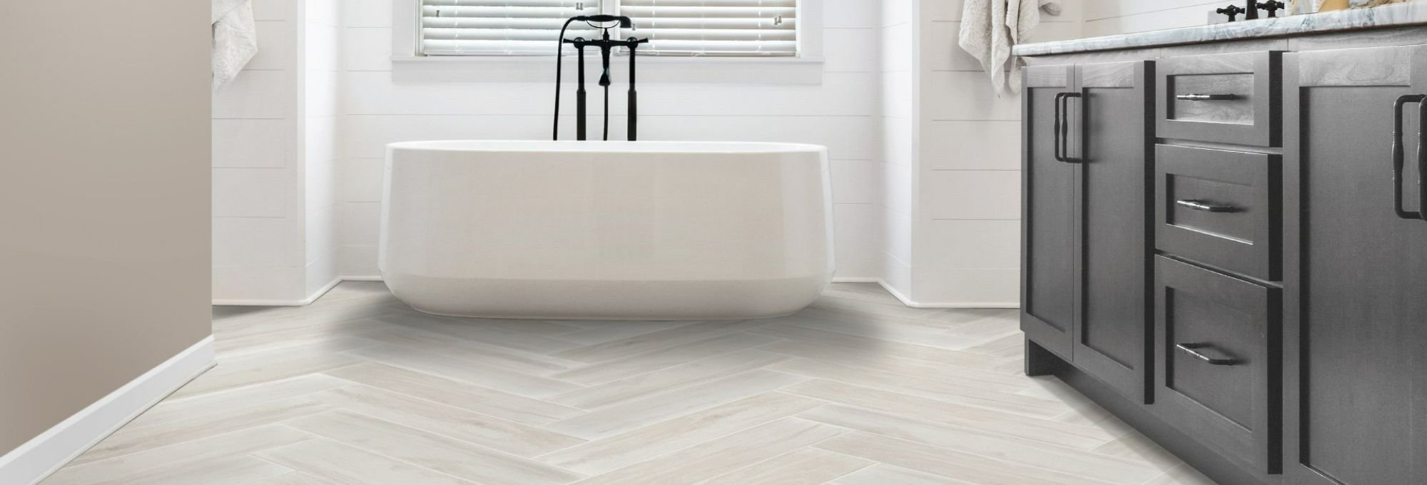 white bathtub and gray cabinet for bathroom with white herringbone style tile floor by Green Carpet Co. - The Flooring Connection in San Antonio, TX